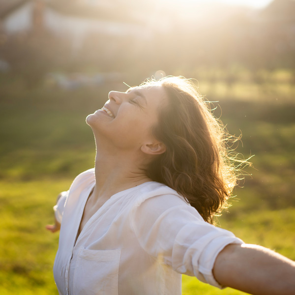 Young caucasian woman enjoying the sun and summer in a green field in the rays of the sun with her arms wide open